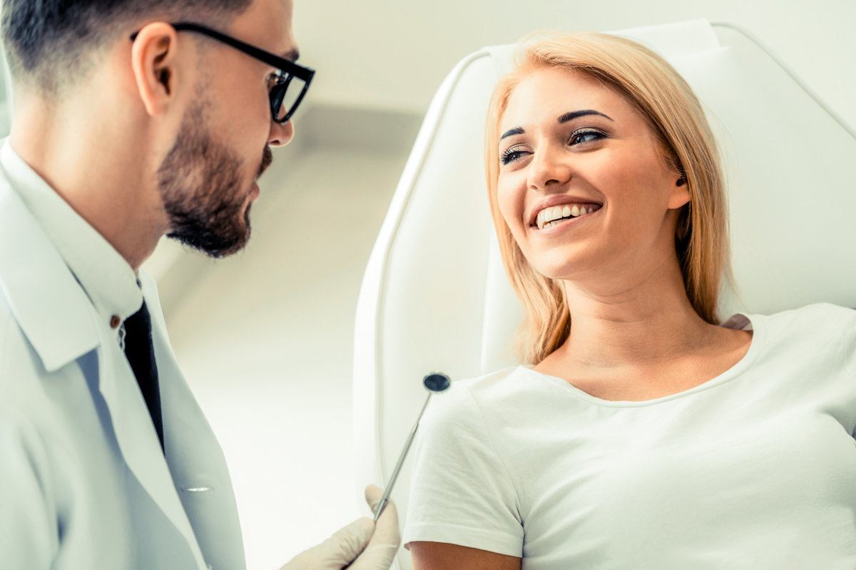 Young handsome dentist talks with happy woman patient sitting on dentist chair in dental clinic. Dentistry care concept.