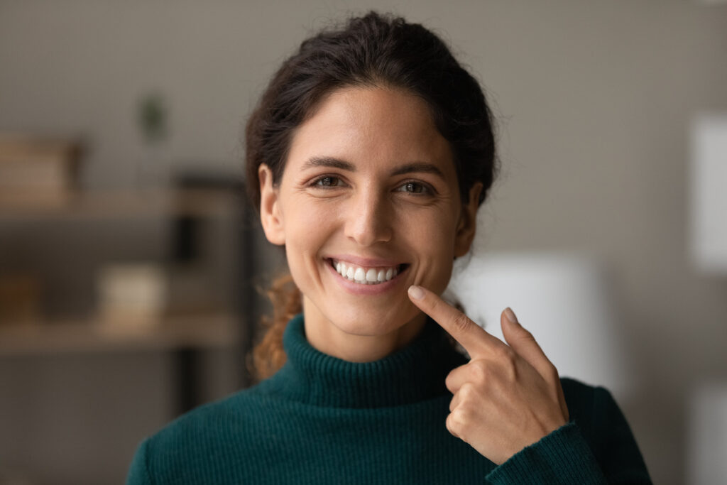 Smiling hispanic lady look at camera point on white teeth