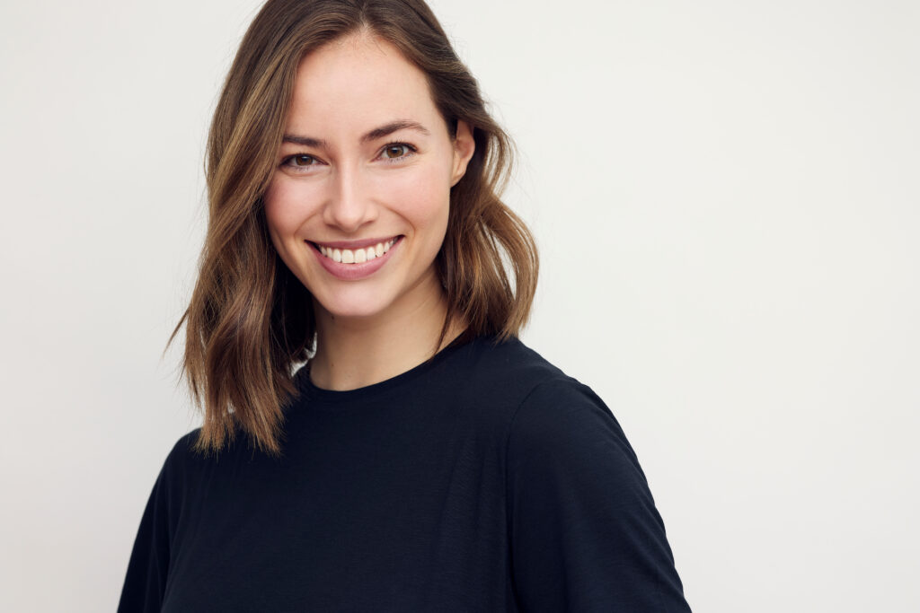 Portrait of beautiful natural brunette woman, smiling and looking in camera with white teeth. Close-up portrait of cute female girl in black t-shirt isolated on white background.