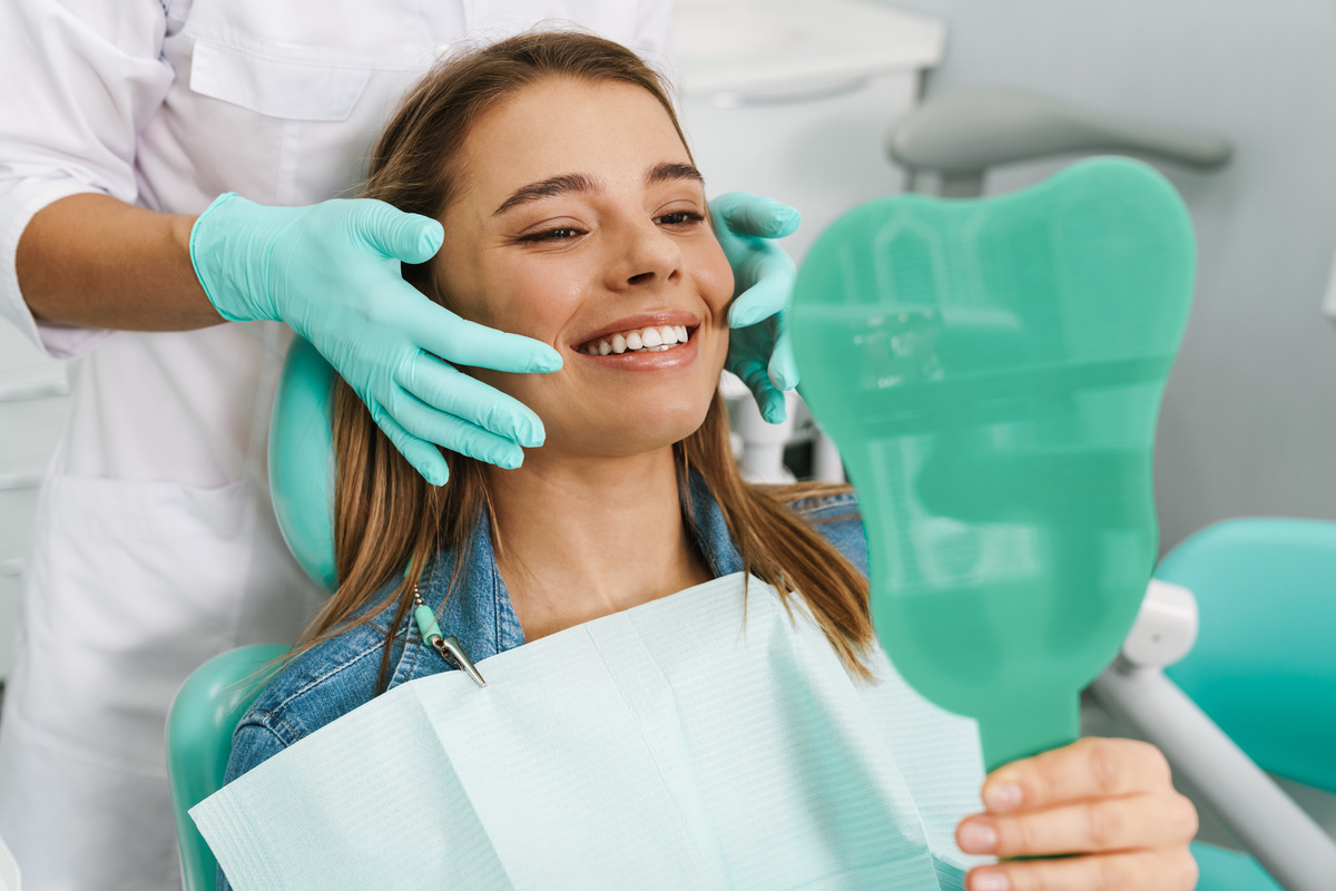 European young woman smiling while looking at mirror in dental clinic
