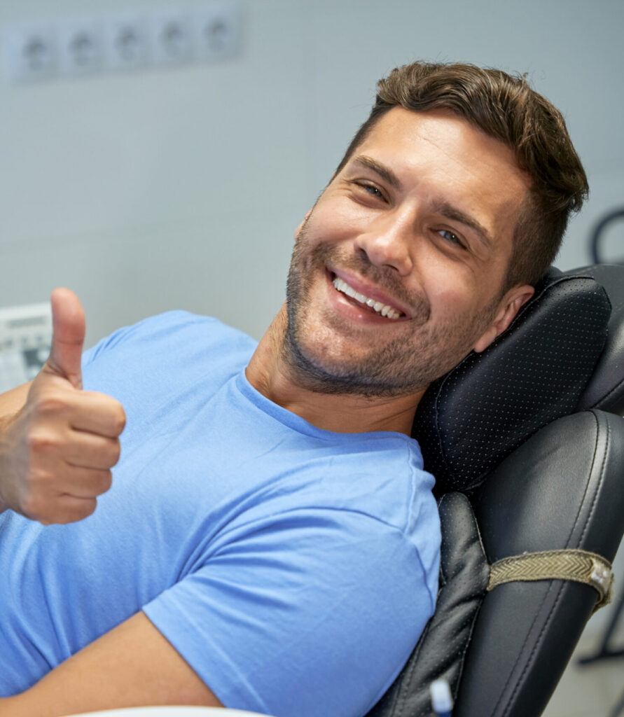 Young brunette man smiling and showing thumbs up while leaning back in a dental chair
