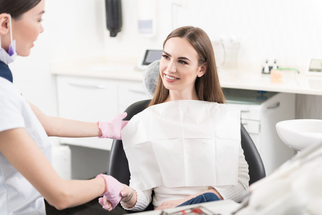 Cheerful patient shaking hands with joyful female dentist standing in apartment