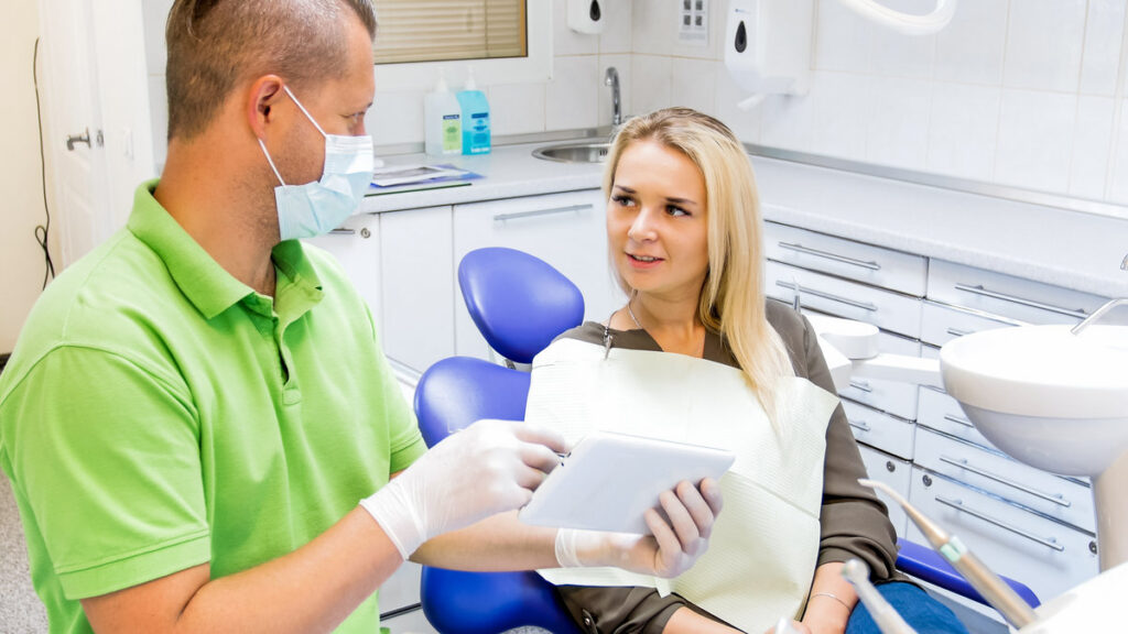 Young woman sitting in dentist chair and talking about treatment with doctor