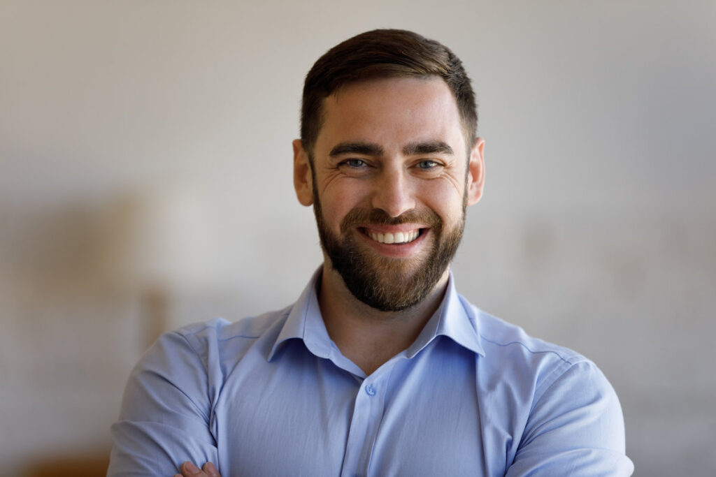 Head shot portrait of smiling confident young bearded man, posing indoors, real estate ownership. Joyful millennial guy showing sincere smile, feeling satisfied with professional dental procedures.