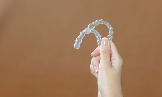 Close-up of a hand holding a clear dental aligner tray