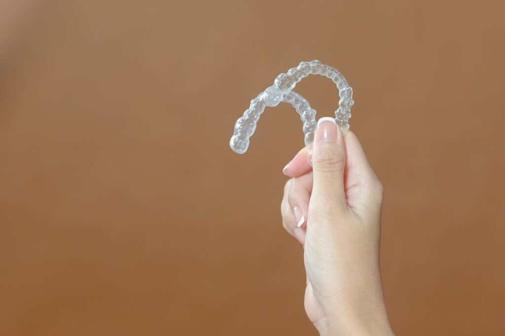 Close up young woman hand is holding Invisalign over brown background
