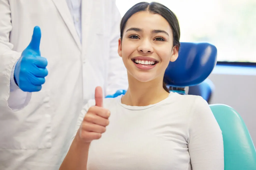 Dentist, client and smile with portrait for thumbs up for success of teeth whitening, oral and dental care. Doctor, assistant and woman with hand gesture for well done or good job, yes and thank you