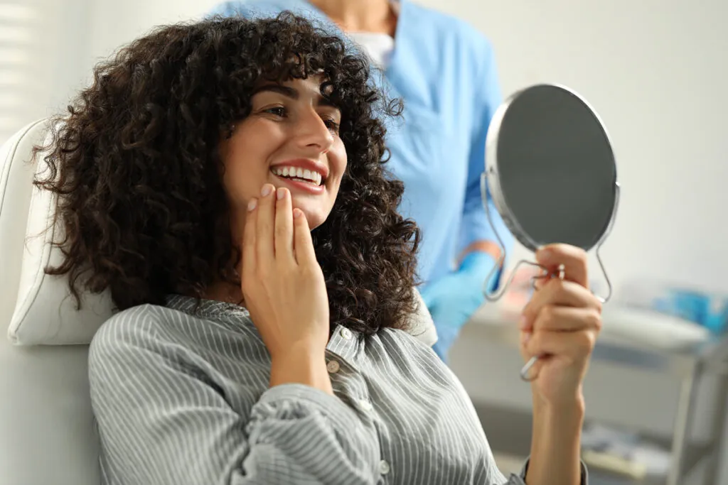 Patient looking in mirror and doctor in clinic, selective focus. Dental veneers