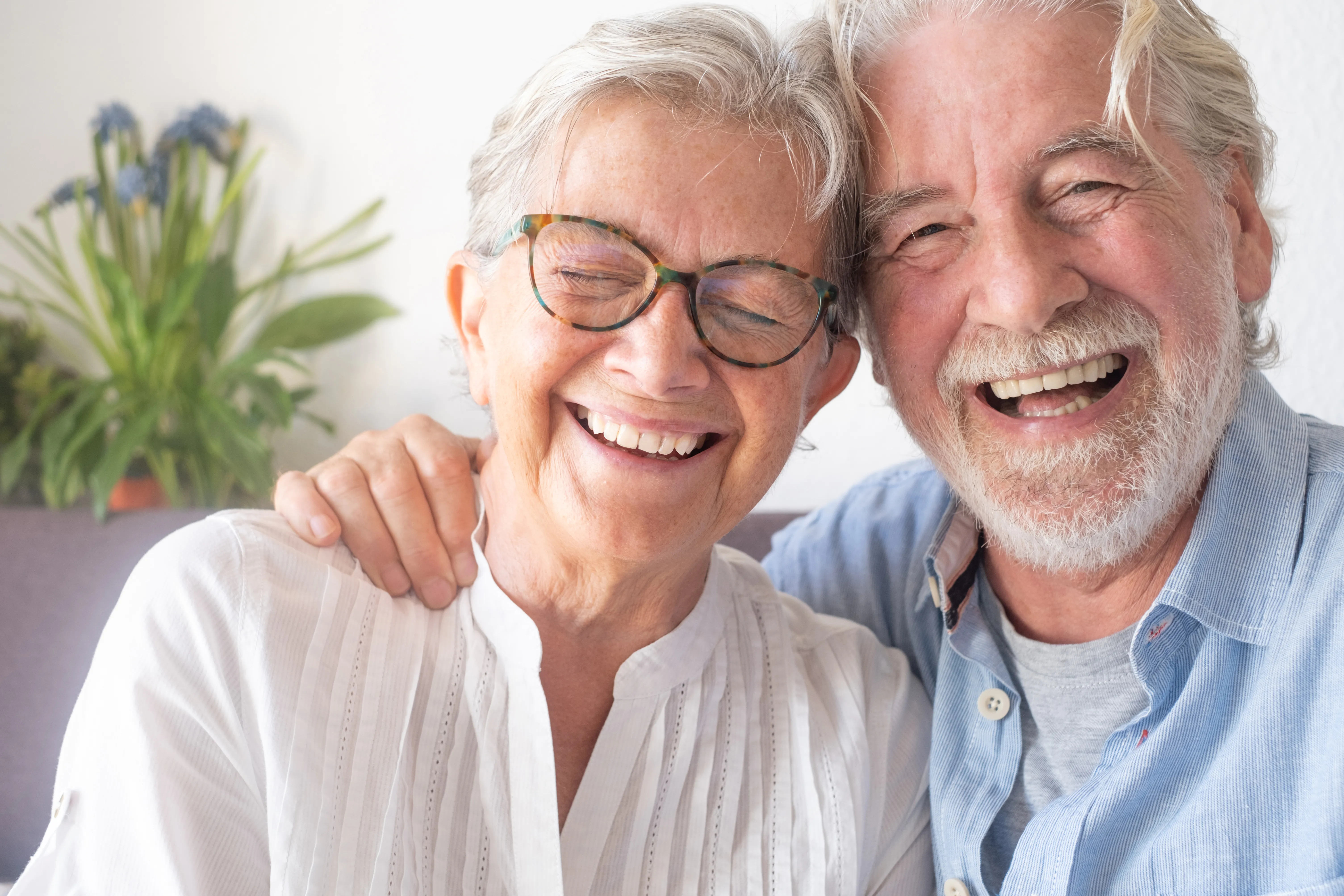 Beautiful senior couple having fun and laughing sitting at home on sofa. Serene elderly people enjoying retirement