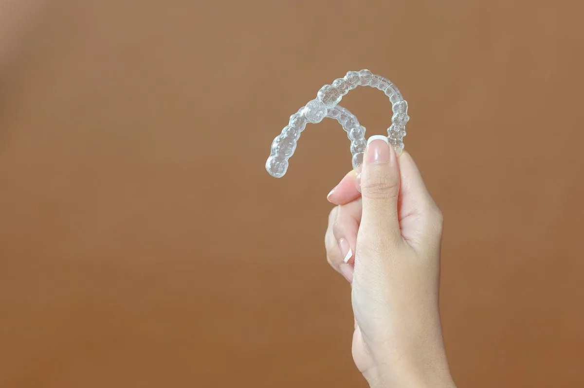 Close up young woman hand is holding Invisalign over brown background